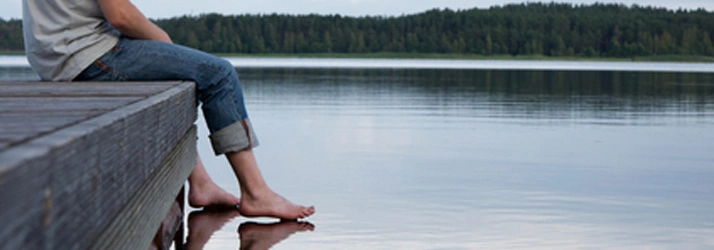Chiropractic Decatur GA Conditions The photo shows a person sitting on a deck with their feet submerged in a beautiful lake.